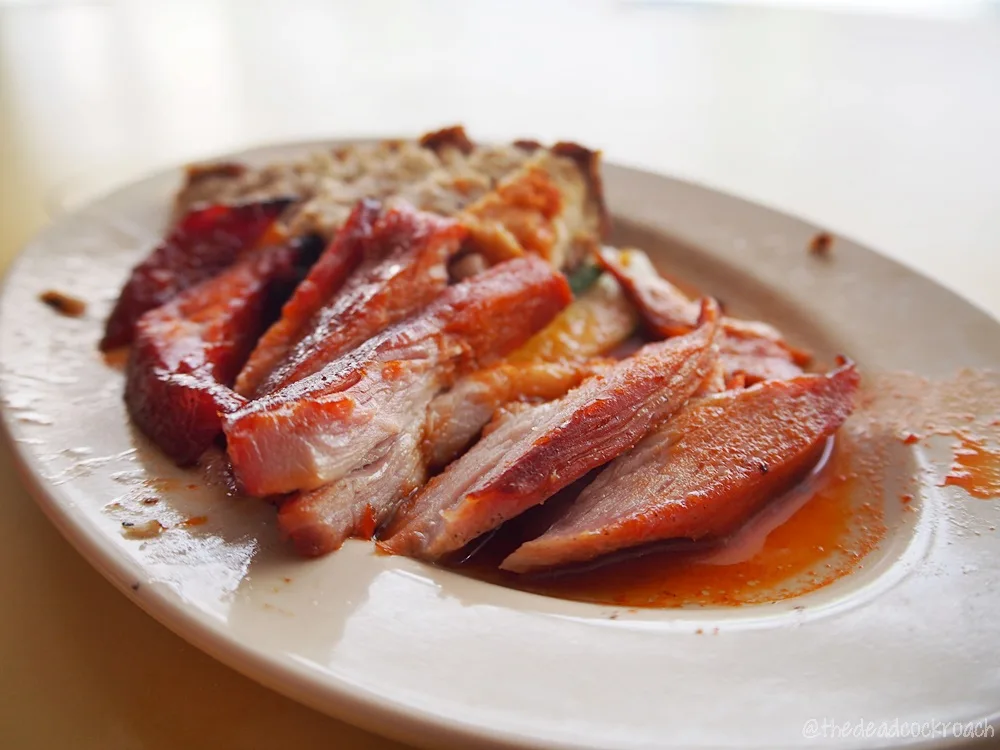 Close-up of Happy World Roast char siew, sliced and glossy with sauce on a white plate