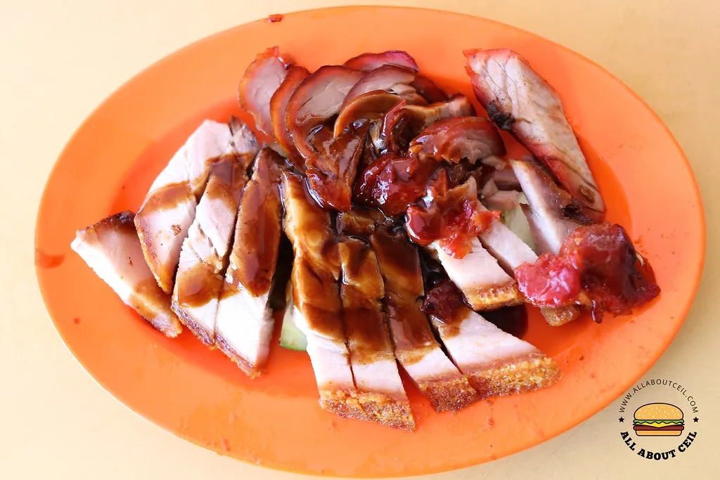 A plate of Happy World Roast char siew and roasted pork belly, sliced and sauced, on an orange melamine plate