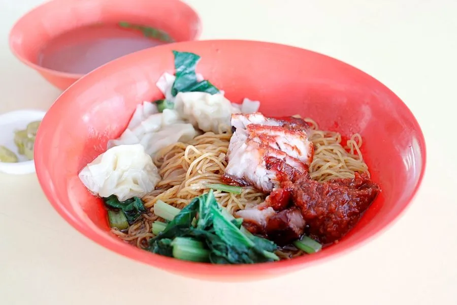 Char siew wanton noodle from Happy World Roast in a red bowl, with wantons, greens and chilli paste