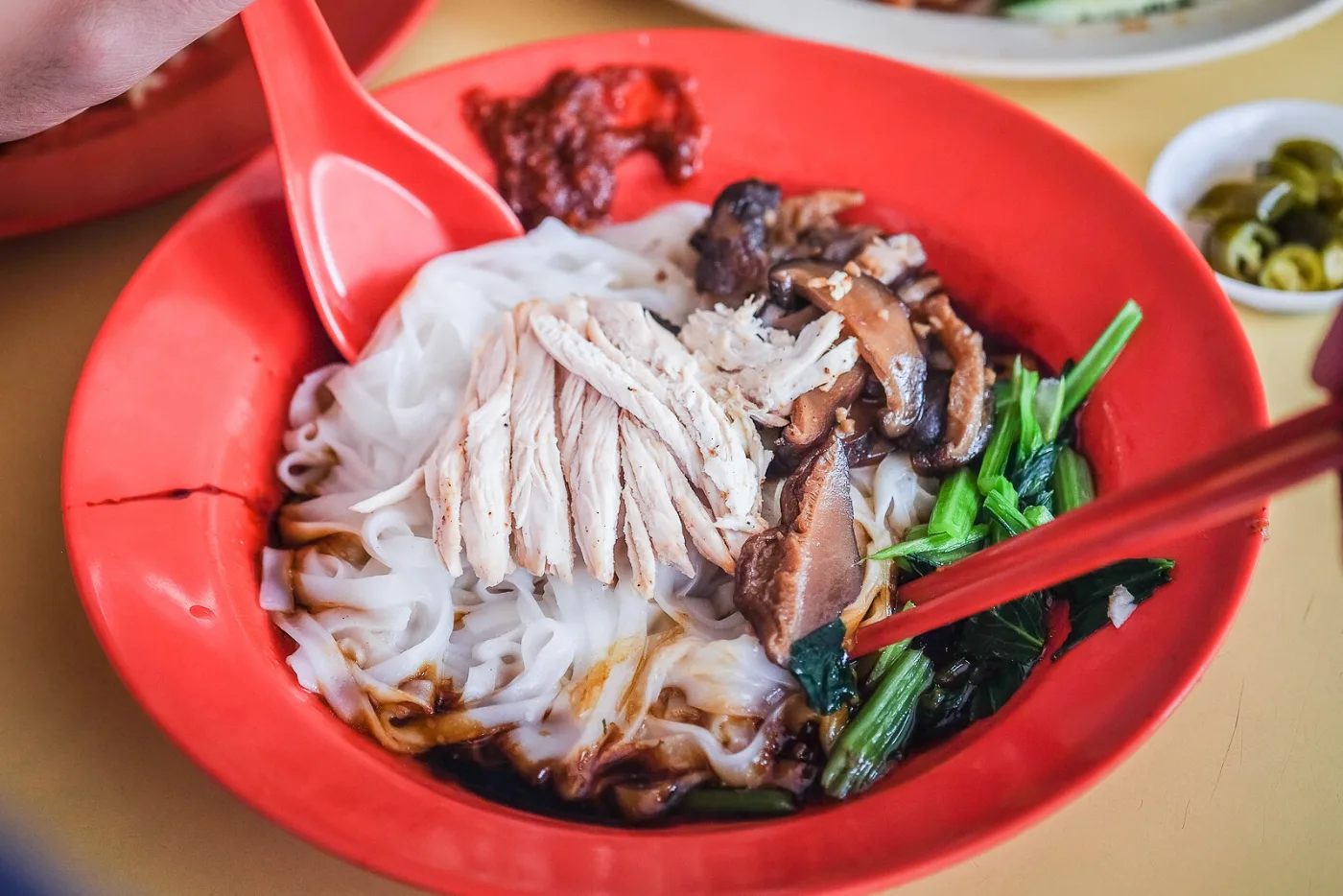Shredded chicken and mushroom hor fun from Happy World Roast in a red bowl with braised mushrooms and greens