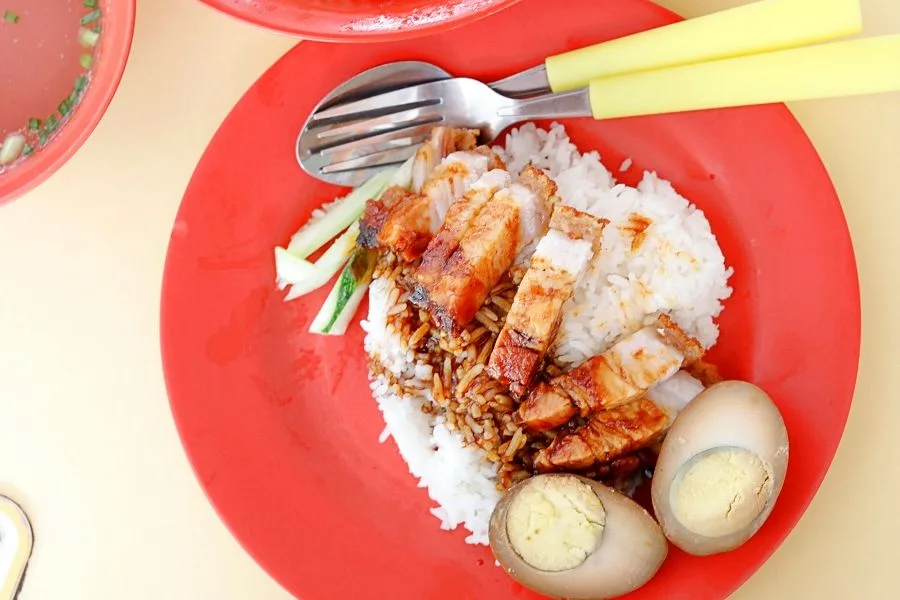 Roasted pork belly rice from Happy World Roast on a red plate with braised eggs, cucumber and dark sauce