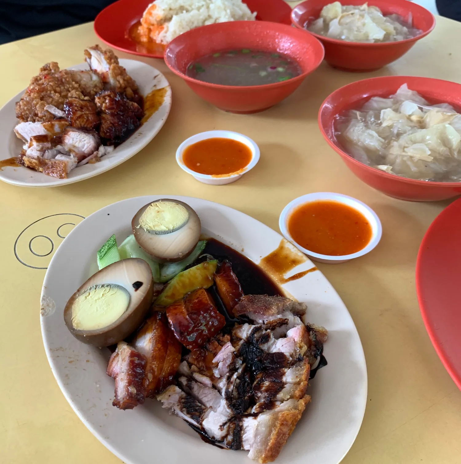 A table of Happy World Roast plates at Empress Road Market: char siew and roasted pork belly with rice, braised eggs, soup and cabbage in red melamine bowls